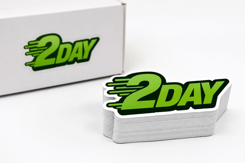Stack of custom die-cut 2Day stickers in front of a shipping box